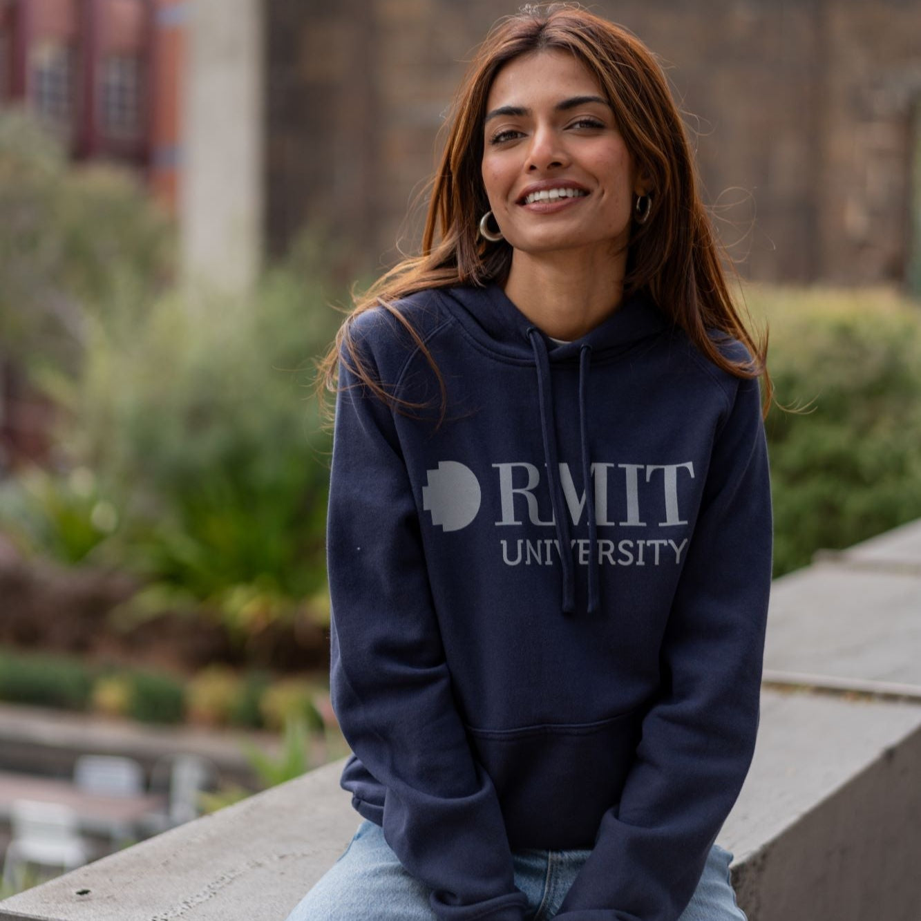 A model showcasing the RMIT Ltd Ed Hoodie in midnight blue from the front view. The hoodie features a printed "RMIT University" logo in light grey, offering a stylish and comfortable fit. Available at the RMIT Store.